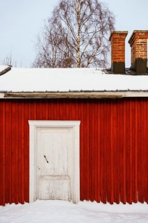 Traditional red wooden cabin against a snow-covered landscape in Swedish Lapland. The rustic