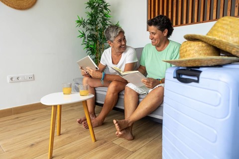 A lesbian couple relaxes on a sofa with a book and a digital tablet, discussing and planning their