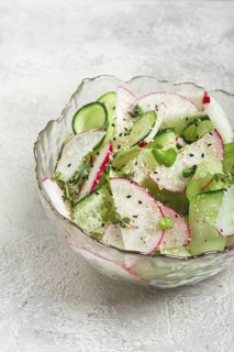A colorful salad featuring sliced cucumbers, radishes, and fresh herbs rests in an elegant bowl.