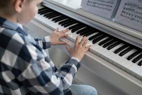 A boy wearing a plaid shirt is playing the piano. The image captures the focused practice session,