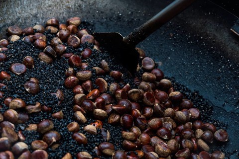 A close-up view of glistening chestnuts being roasted on a large metal pan, showcasing a
