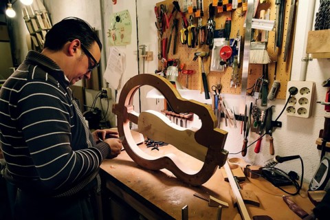A luthier focuses on crafting a bass guitar in a workshop filled with essential tools. The
