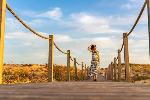 Woman walking on a wooden boardwalk leading through sand dunes to the beach in seignosse le penon,