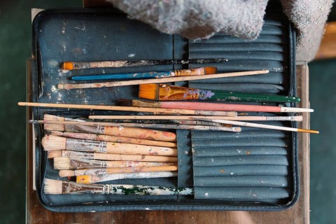 A set of well-worn paintbrushes, covered in dried paint, rests in a fabric case on an artist's