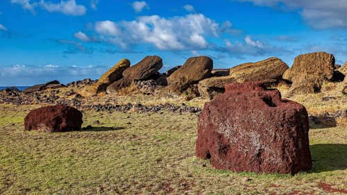 Two reddish stones in a landscape with fallen moai under cloudy sky, the moai statues on Easter