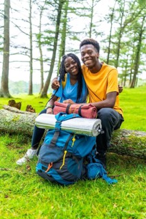 Vertical portrait of a cute young african couple embracing sitting on a log in a green beauty