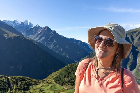 Smiling woman wearing a hat and sunglasses enjoys a scenic trek in the Everest region, with