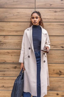 Vertical portrait of a young african american businesswoman in coat holding mobile and laptop bag