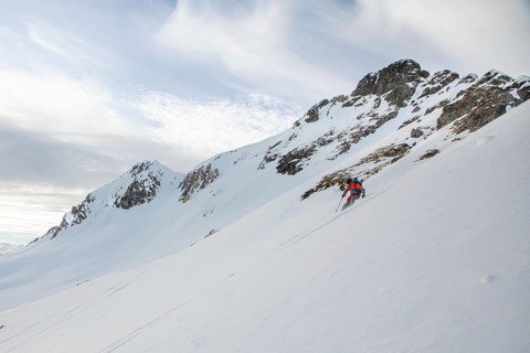 A skier descends a steep snowy slope under a partly cloudy sky. This image captures the essence of