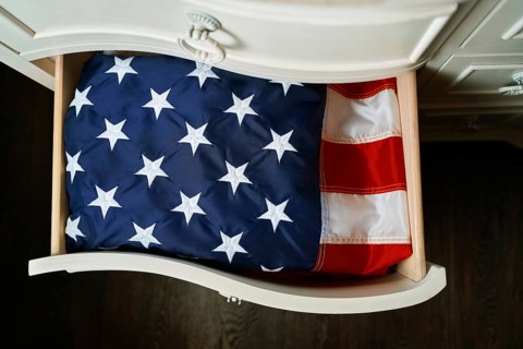 A neatly folded American flag in a partially opened wooden drawer, showcasing its stars and stripes