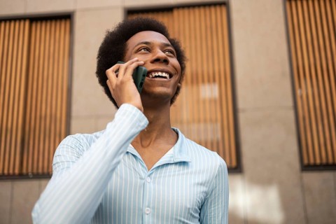 A joyful non-binary person talks on the phone outdoors, symbolizing identity, freedom, and pride.