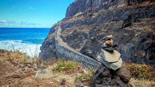 Stone tower, stone men on the edge of a cliff path with a view of the blue sea under a blue sky,