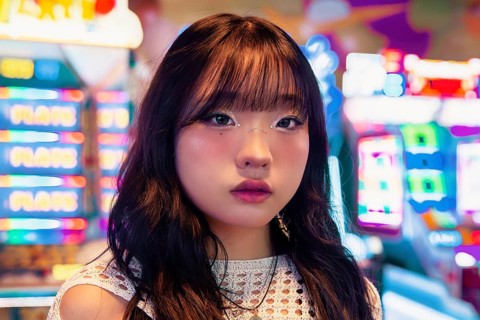 An Asian Gen Z girl with stylish makeup and hair stands in an arcade, surrounded by colorful lights
