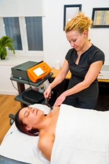 Vertical side view of a female beauty patient lying on massage table receiving indiba treatment