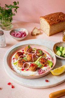 A beautifully arranged plate of meatballs garnished with sliced red onions, greens, and pomegranate
