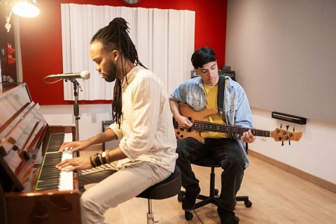 Two musicians collaborate in a professional recording studio, with one playing the piano and the