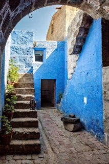 A sunny courtyard with blue walls, stone arches, stairs and lush plants that create a Mediterranean