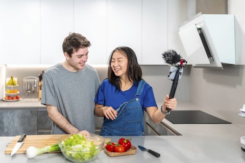 Happy multiethnic couple preparing a salad and recording a cooking show video in a modern kitchen