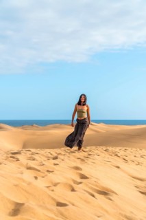 Young woman enjoying her vacation walking barefoot on the sand dunes of maspalomas with the ocean