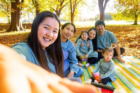 Happy Asian family having a joyful picnic outdoors, sitting on a blanket surrounded by autumn