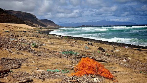 Dirty beach with trash, plastic waste and old fishing nets, waves in cloudy skies, Calhau hiking,
