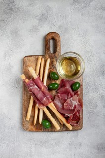 An appetizer of prosciutto, grissini and olives, served on a wooden board, with olive oil