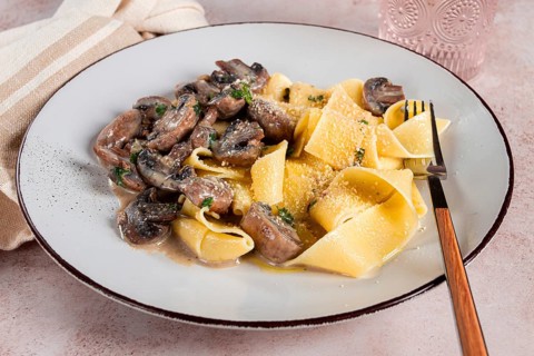 Delicious pappardelle pasta with mushrooms and cream served on a white plate