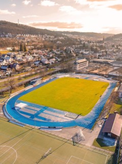 Stadium with blue running track in urban surroundings, surrounded by hills and residential houses,