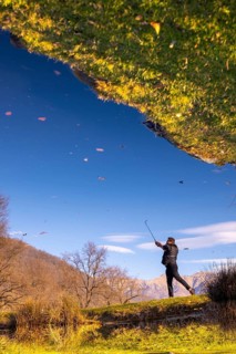 Male Golfer Reflected in a Water Pond and Hitting the Golf Ball on Fairway on Golf Course with