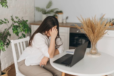 A nutritionist sits at a table, thoughtfully analyzing data on a laptop. The modern kitchen setting