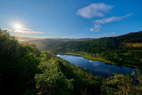 A lake in a green landscape illuminated by the rising sun, Queens View, Fincastle, Pitlochry,