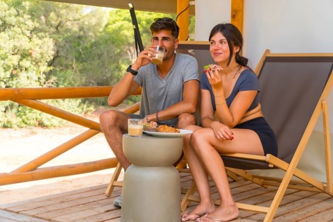 Young couple enjoying a leisurely breakfast on the terrace of their glamping tent, surrounded by