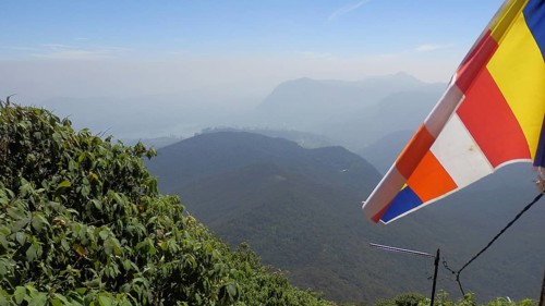 Colourful Buddhist flag fluttering in the wind over a vast mountain landscape under clear sky, view