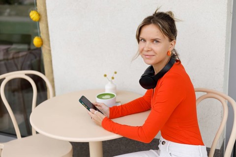 A woman in Warsaw sits at an outdoor cafe She is using her smartphone, with headphones around her