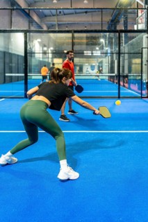 Woman striking a pickleball on a bright blue indoor court, focused and powerful in motion,
