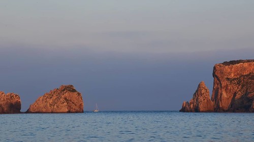 Rocky coast at sunrise with a boat in calm sea, morning light, Tsichli Babas islet, Sfaktiria