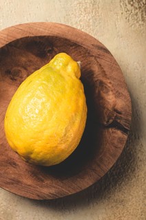 A vibrant yellow lemon sits atop a rustic wooden plate, showcasing its bumpy texture and bright
