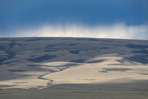 Sunlight and cloud shadows on vast steppe hills, rising rain clouds over the horizon, Patagonia,