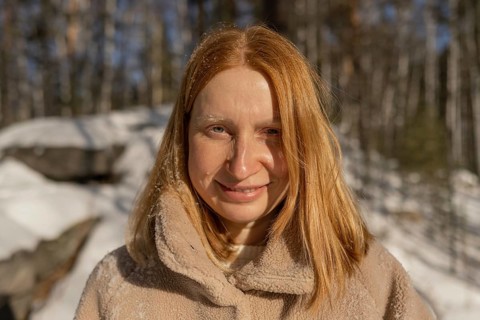 A smiling red hair woman looking at camera in a cozy jacket stands in a snowy forest, basking in