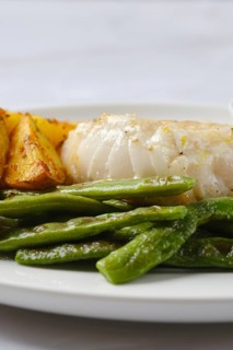 A plate showcases tender white fish alongside perfectly roasted golden potatoes and vibrant green