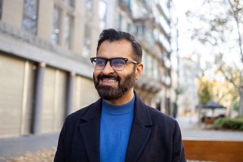 A cheerful Indian businessman in a stylish winter coat and sweater smiles gently while looking away