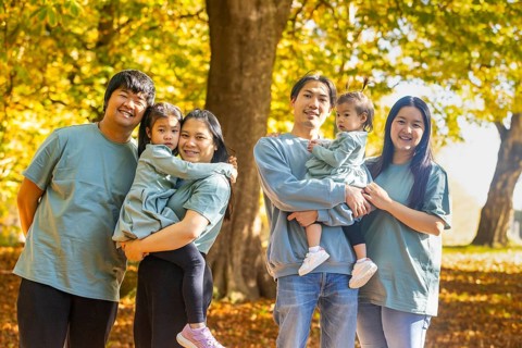 An Asian family enjoying a sunny day at the park, surrounded by lush trees and vibrant foliage. Two