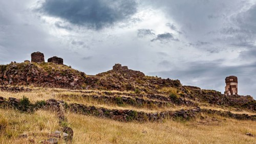 Ancient stone ruins on a grassy hill under a cloudy sky, The Chullpas of Sillustani near Puno in