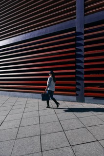 A woman in casual attire walks by a modern building with distinctive horizontal slats. The