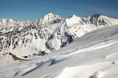 Stunning panoramic view of snow-covered mountain peaks under a clear blue sky, showcasing a