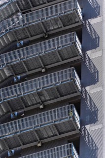 A series of sleek metal staircases adorn the exterior of an urban high-rise building, casting