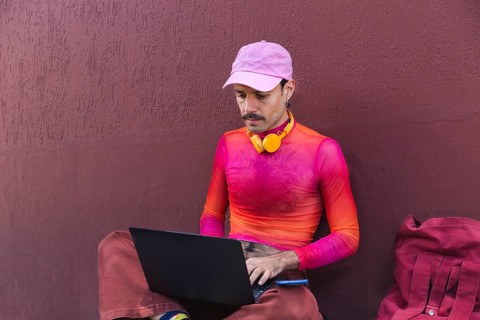 In Quito, Ecuador, a young Spanish man in pink clothing works on his laptop outdoors against a
