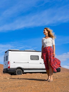 A woman stands confidently next to a white van amidst the stunning landscapes of Fuerteventura,