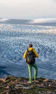Young man, tourist in front of impressive glacier, in the evening light, glacier tongues