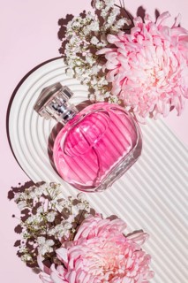 Pink perfume bottle paired with lush pink flowers on a textured white base, capturing a sense of